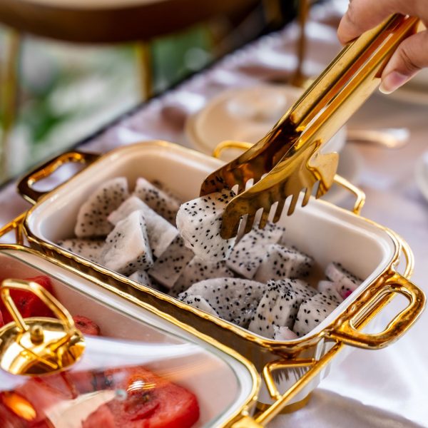 A close-up of a hand elegantly serving diced dragon fruit from a golden-trimmed serving dish, highlighting fresh dining at Golden Beach Resort.